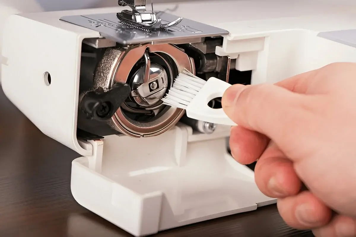 A person using a small brush to clean lint from the bobbin area of th Janome sewing machines.