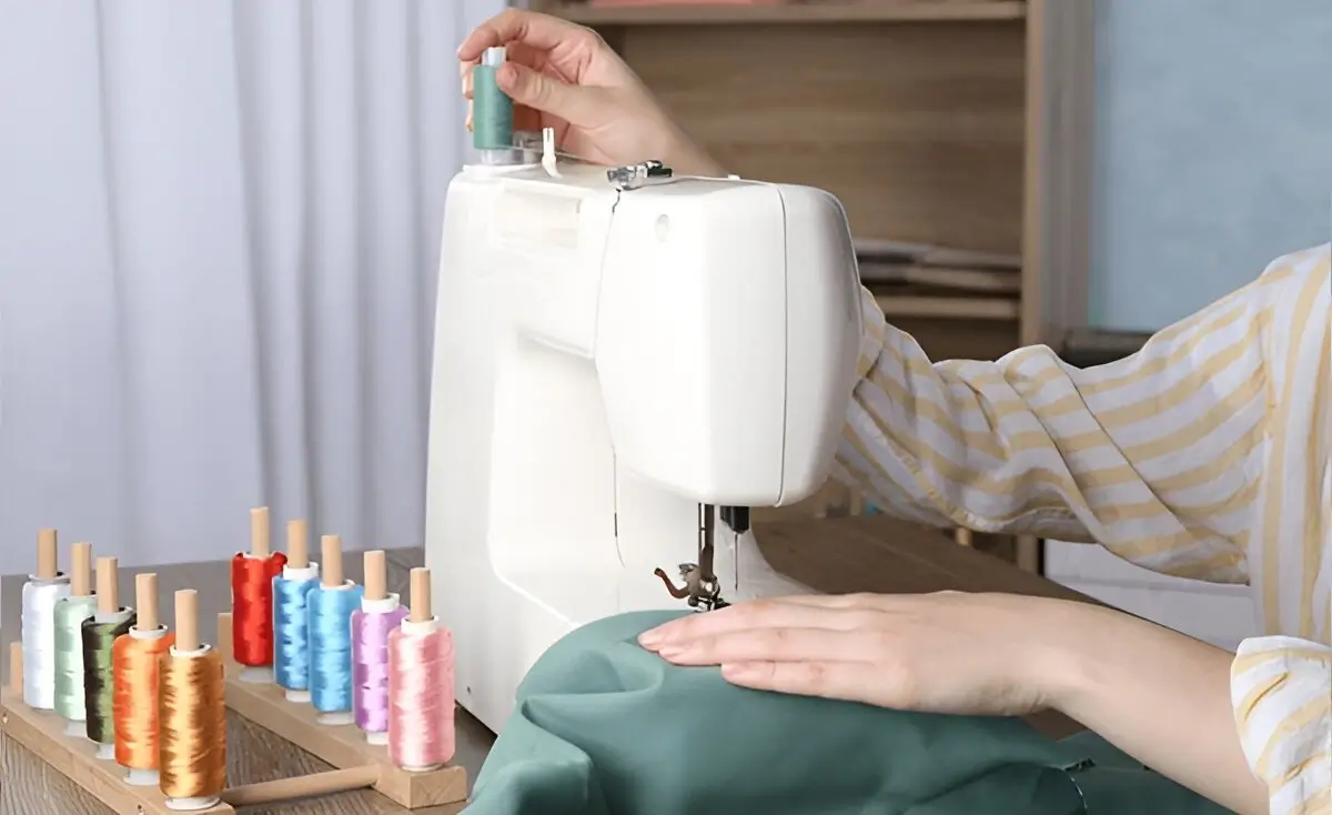 A woman smiling while sewing on a modern Janome sewing machine in a bright craft room.